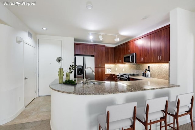 kitchen with light tile patterned floors, kitchen peninsula, stainless steel appliances, backsplash, and sink