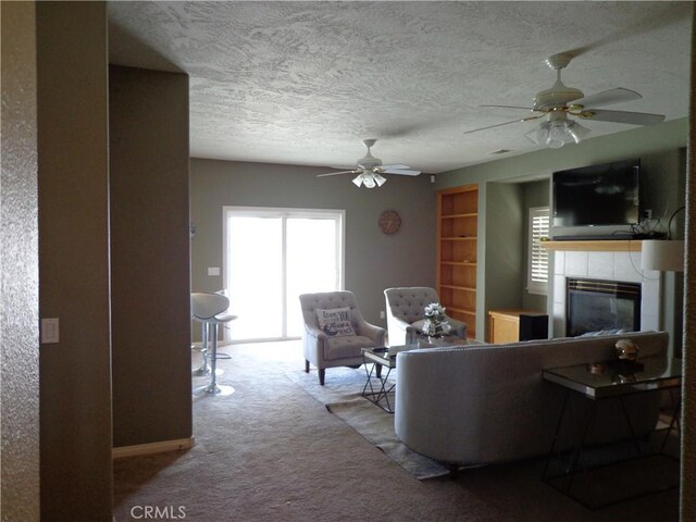 living room with ceiling fan, light colored carpet, a textured ceiling, and a tiled fireplace