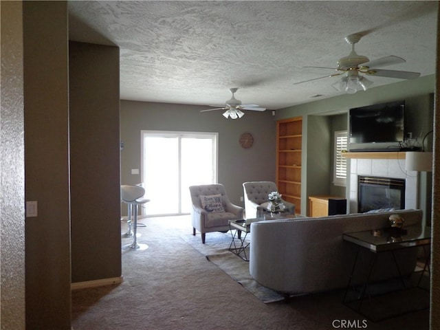 carpeted living room featuring a tiled fireplace, ceiling fan, and a textured ceiling