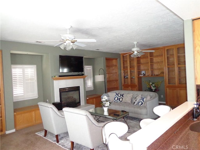 living room with a tile fireplace, ceiling fan, light colored carpet, and a textured ceiling