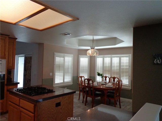 kitchen with a center island, black appliances, a raised ceiling, hanging light fixtures, and a chandelier