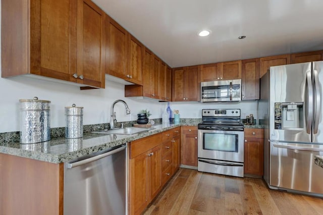 kitchen with light stone countertops, sink, stainless steel appliances, and light wood-type flooring