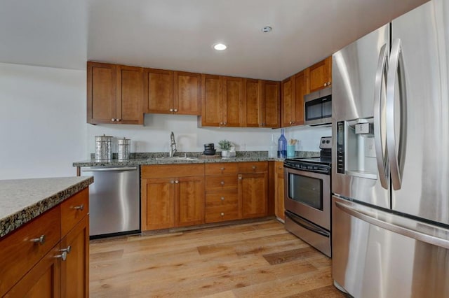 kitchen featuring appliances with stainless steel finishes, sink, stone counters, and light hardwood / wood-style floors