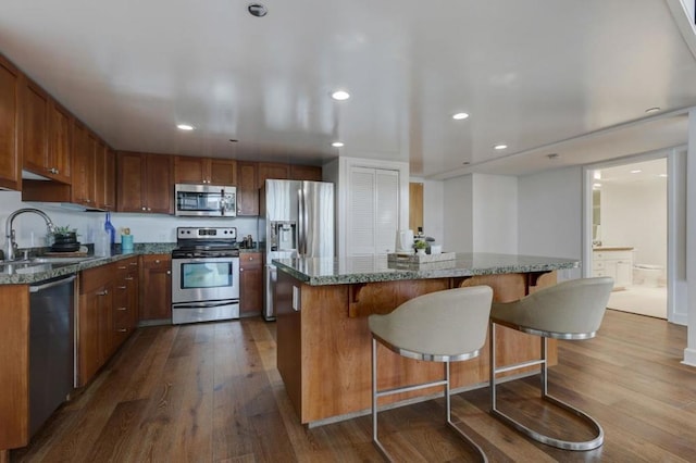 kitchen featuring stainless steel appliances, wood-type flooring, a kitchen island, and sink