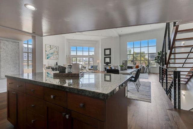 kitchen with dark wood-type flooring, a kitchen island, and dark stone countertops