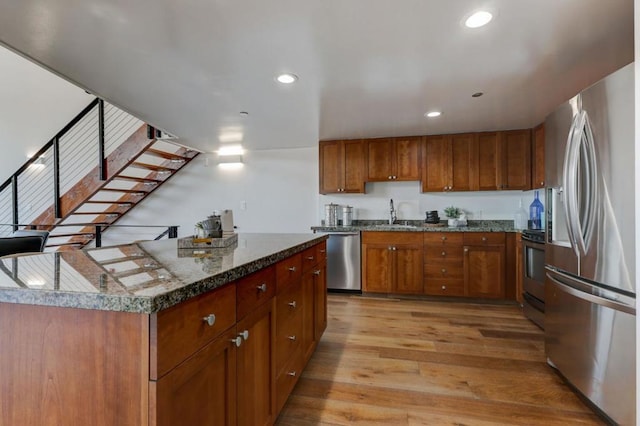 kitchen featuring dark stone countertops, a center island, sink, light hardwood / wood-style flooring, and appliances with stainless steel finishes