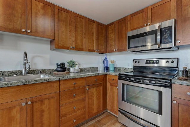 kitchen with light stone countertops, sink, stainless steel appliances, and light wood-type flooring