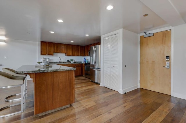 kitchen with light hardwood / wood-style floors, appliances with stainless steel finishes, a kitchen breakfast bar, dark stone counters, and sink