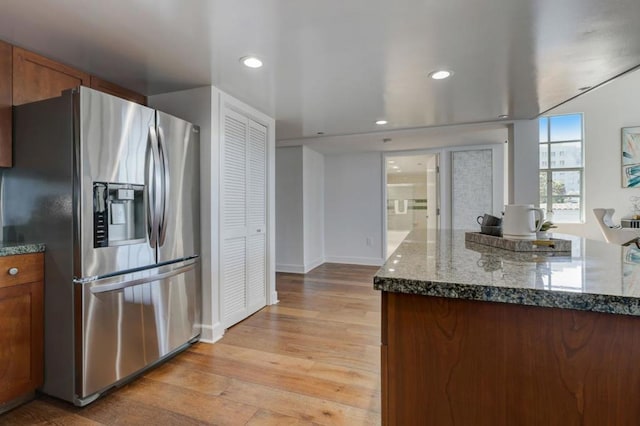 kitchen with stainless steel fridge with ice dispenser, dark stone countertops, and light hardwood / wood-style flooring