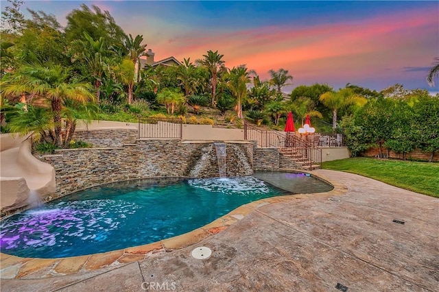 pool at dusk featuring pool water feature and a patio area