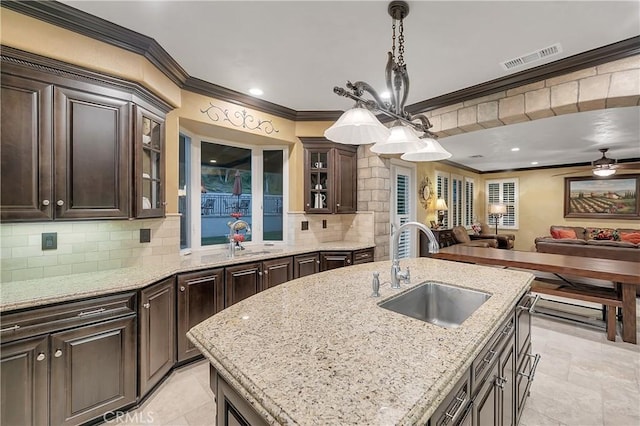 kitchen featuring backsplash, a center island with sink, sink, crown molding, and hanging light fixtures