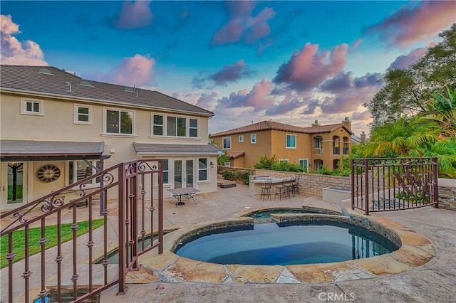 pool at dusk with an in ground hot tub, a patio area, and exterior bar