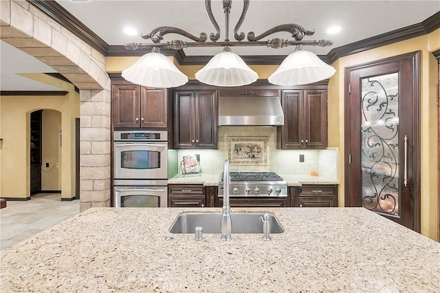 kitchen with extractor fan, stainless steel double oven, tasteful backsplash, ornamental molding, and light stone counters