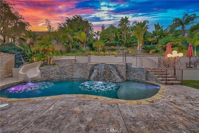 pool at dusk featuring a patio and a water slide