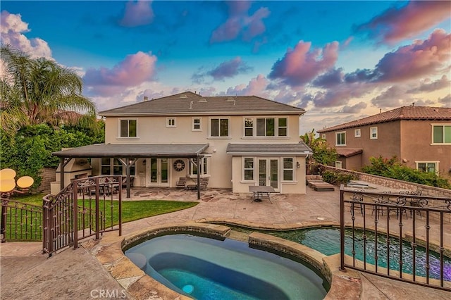 back house at dusk with a patio area, exterior bar, and a swimming pool with hot tub