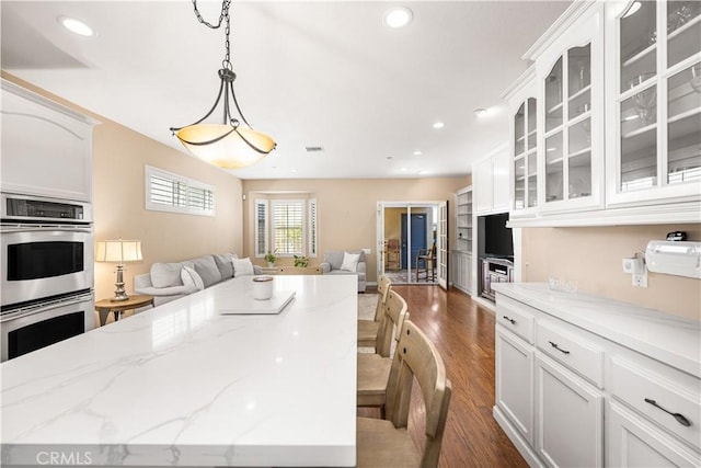 kitchen with pendant lighting, white cabinets, dark wood-type flooring, and stainless steel double oven