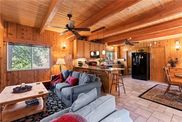 living room featuring ceiling fan, beam ceiling, and wooden walls