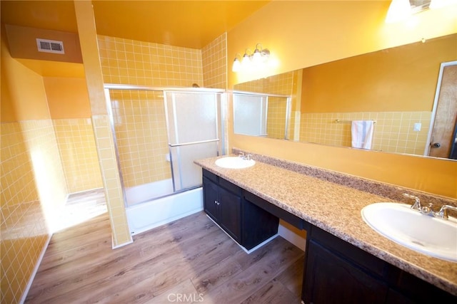 bathroom with vanity, shower / bath combination with glass door, hardwood / wood-style floors, and tile walls