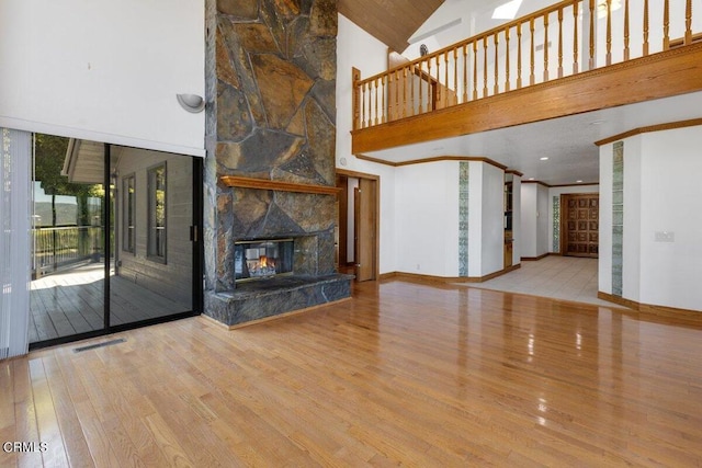 unfurnished living room featuring hardwood / wood-style floors, high vaulted ceiling, and a stone fireplace