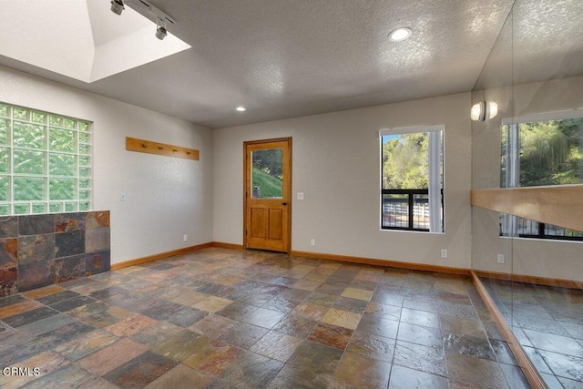 interior space with a skylight, dark tile floors, track lighting, and a textured ceiling