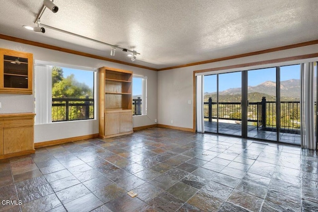 tiled empty room featuring a mountain view, track lighting, a wealth of natural light, and a textured ceiling