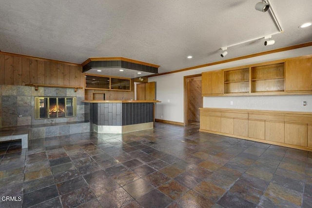 interior space featuring crown molding, a tiled fireplace, track lighting, dark tile flooring, and a textured ceiling