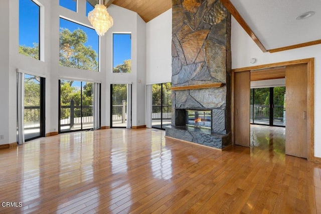 unfurnished living room featuring wood-type flooring, a fireplace, high vaulted ceiling, and an inviting chandelier