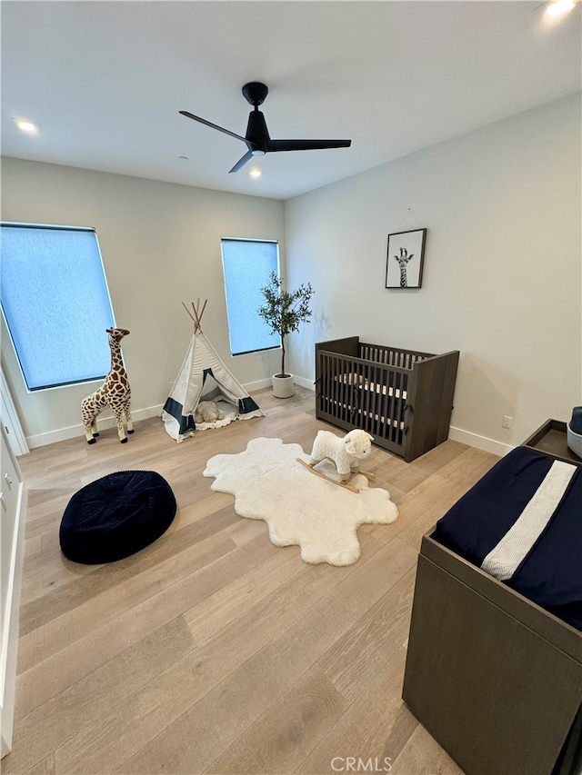 bedroom featuring a crib, light hardwood / wood-style floors, and ceiling fan