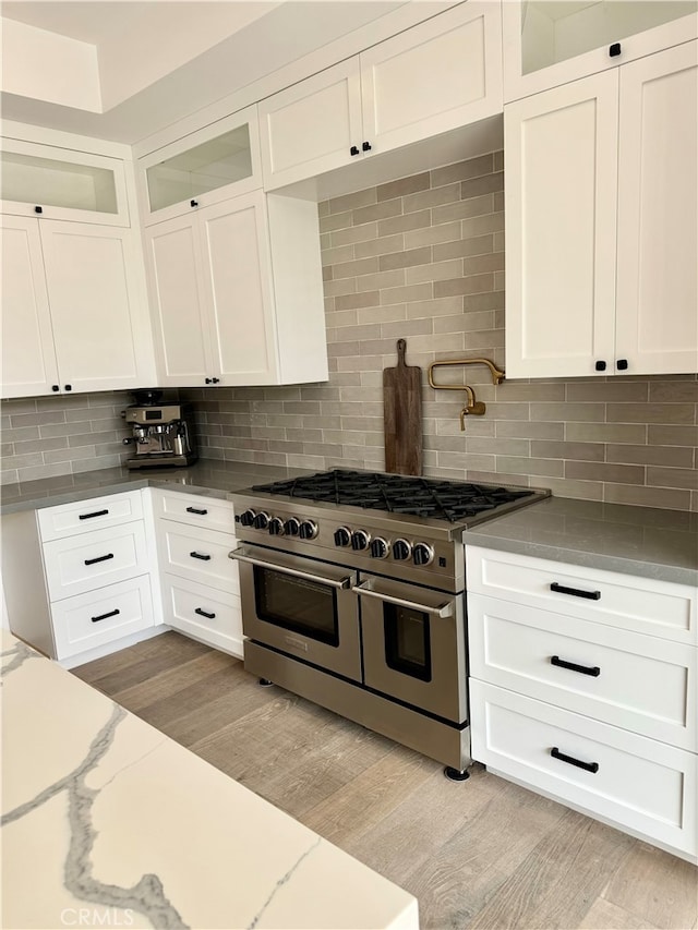 kitchen with range with two ovens, backsplash, light wood-type flooring, and white cabinets