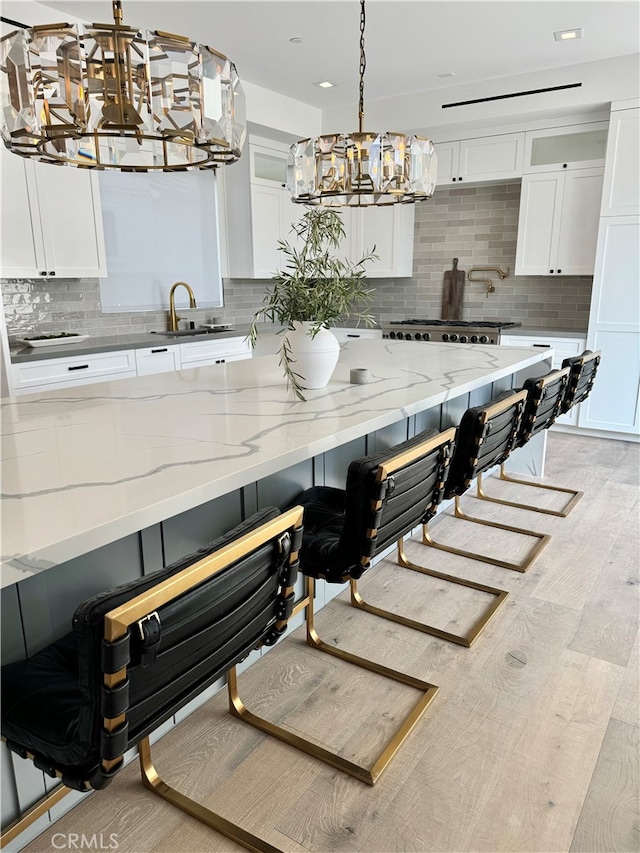 kitchen with a kitchen breakfast bar, decorative backsplash, decorative light fixtures, and white cabinetry