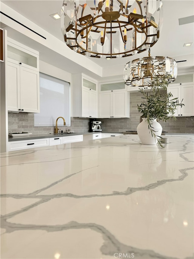 kitchen featuring decorative backsplash, light stone countertops, and white cabinets