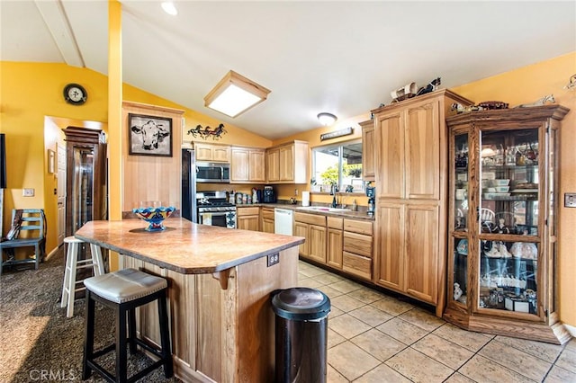 kitchen featuring a breakfast bar, sink, stainless steel appliances, vaulted ceiling, and light brown cabinetry