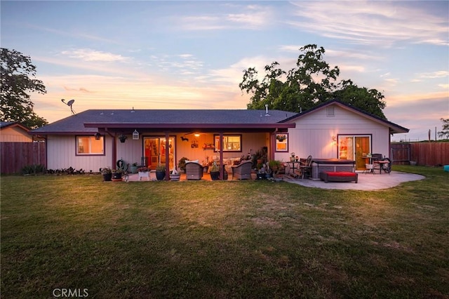 back house at dusk with a yard, a hot tub, and a patio area