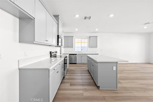 kitchen with stainless steel appliances, a center island, light hardwood / wood-style flooring, and gray cabinets