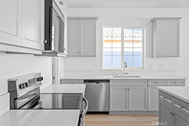 kitchen with light wood-type flooring, stainless steel appliances, sink, and gray cabinetry