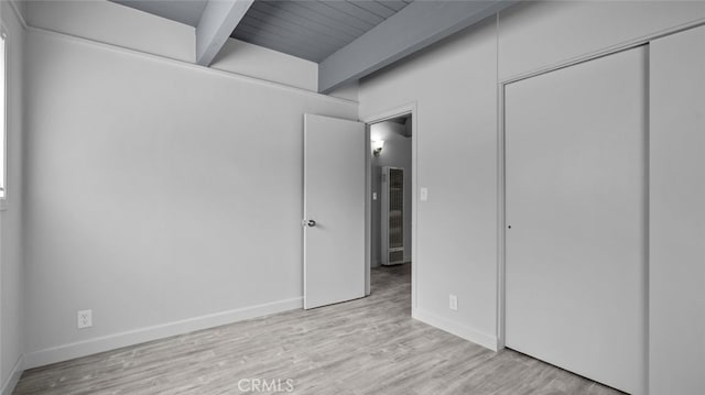 unfurnished bedroom with beam ceiling, light hardwood / wood-style flooring, wooden ceiling, and a closet