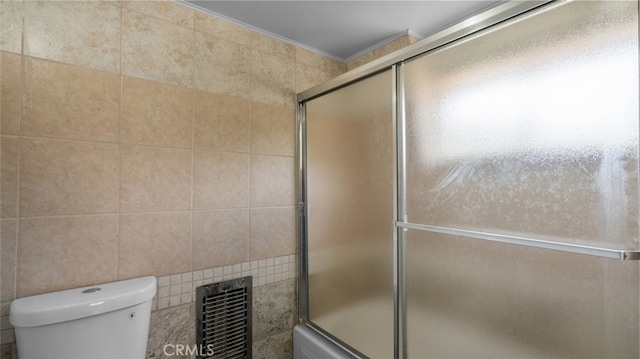 bathroom featuring combined bath / shower with glass door, tile walls, and toilet