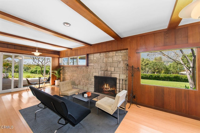 living room with beamed ceiling, wood walls, a stone fireplace, and hardwood / wood-style flooring