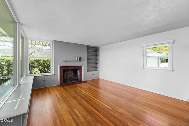 unfurnished living room featuring hardwood / wood-style floors, a textured ceiling, a fireplace, and built in shelves