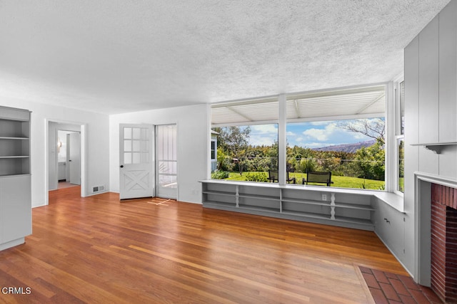 unfurnished living room featuring built in features, wood-type flooring, a brick fireplace, and a textured ceiling