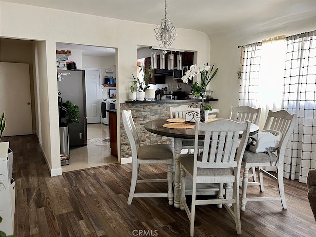 dining area with hardwood / wood-style floors, independent washer and dryer, and an inviting chandelier