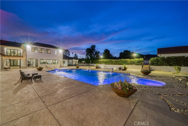 pool at dusk with pool water feature and a patio