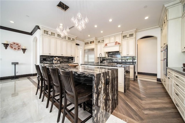 kitchen with hanging light fixtures, a center island with sink, parquet floors, stainless steel appliances, and cream cabinetry