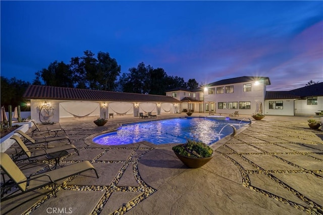 pool at dusk featuring a patio and pool water feature