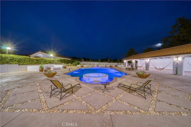 pool at twilight featuring pool water feature, a jacuzzi, and a patio