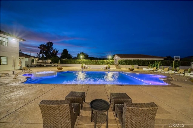 pool at dusk featuring an in ground hot tub and a patio