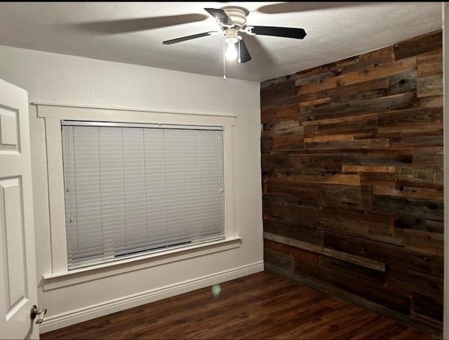 unfurnished room with ceiling fan, dark hardwood / wood-style floors, a textured ceiling, and wooden walls