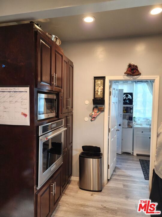 kitchen featuring built in microwave, oven, dark brown cabinets, and light hardwood / wood-style floors