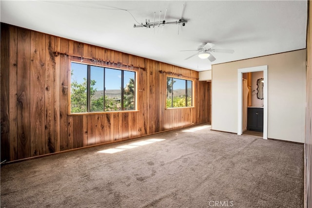 unfurnished room featuring carpet floors, ceiling fan, and wood walls