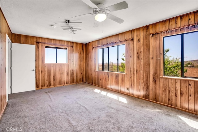 empty room featuring carpet, ceiling fan, and wooden walls